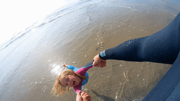 Papa wirbelt seine Tochter am Strand herum, während er mit der Insta360 GO 3 filmt, der besten kleinen Familienkamera.