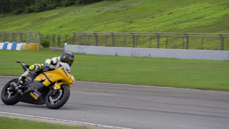 A motorcyclist taking a turn on a motorcycle track with an Insta360 camera mounted on the tail