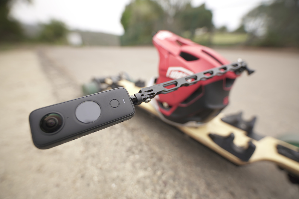 A longboard on the ground with a helmet, which has the Unicorn Mount attached to it, with the Insta360 ONE X2 camera mounted on the end.