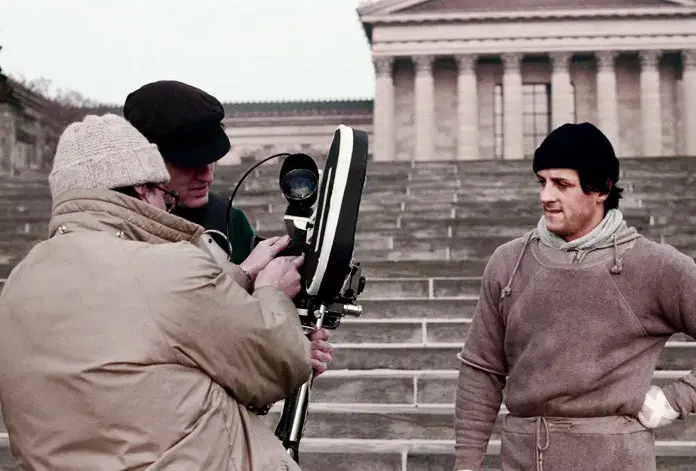 Sylvester Stallone and two camera operators on the steps of the Philadelphia Museum of Art, looking at a steadicam rig.