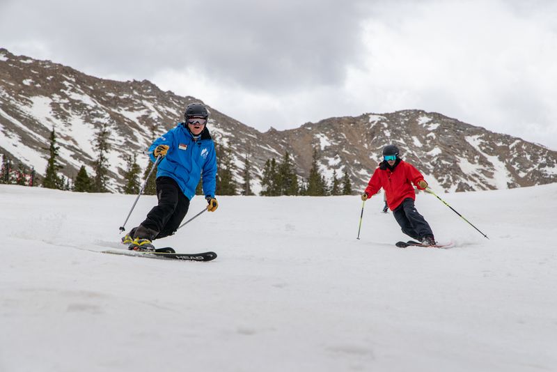 Two skiers skiing down a mountain. One is wearing red and the other is wearing blue.