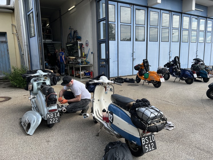 A man surrounded by classic scooters, bent down trying to fix one.