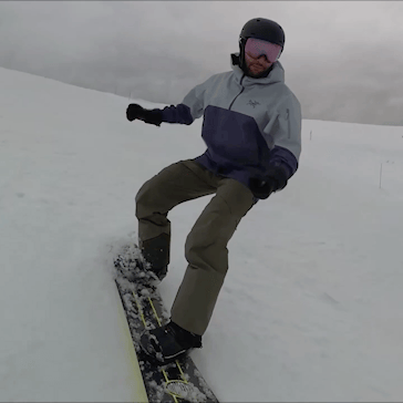 A snowboarder snowboarding down a mountain with action camera Insta360 X4 attached to a selfie stick. There is a green arrow on screen next to his board indicating the lack of an edge change.