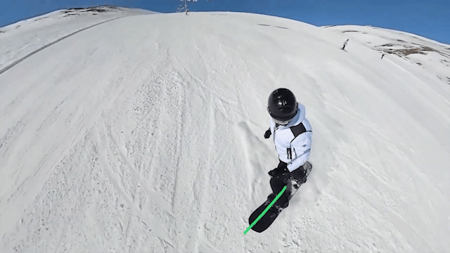 A snowboarder snowboarding down a mountain with action camera Insta360 X4 attached to a selfie stick. There are 2 green arrows about 90 degrees apart on the screen indicating the lack of an edge change.