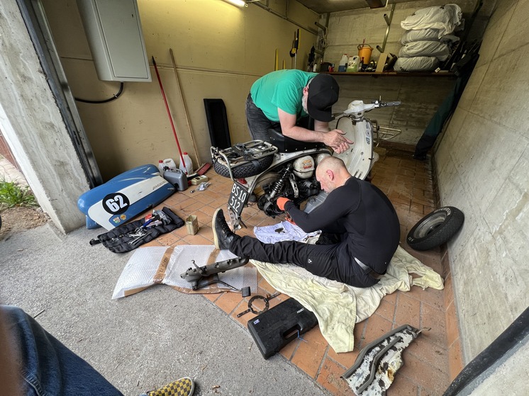 Two men fixing a scooter in a garage.