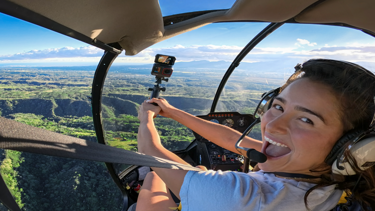 One woman in helicopter holds a camera smiling.