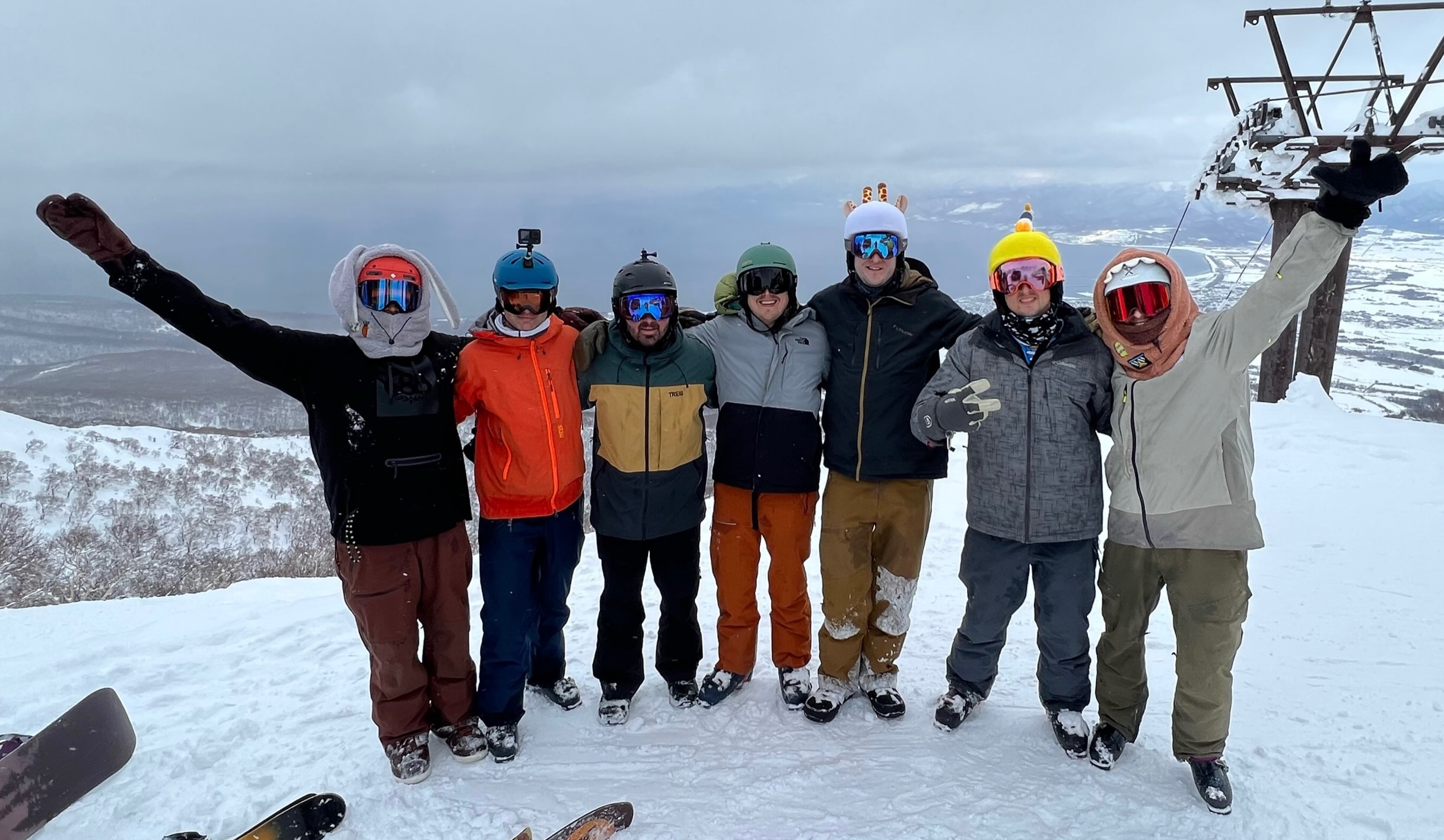 A group of friends in skiing and snowboarding gear posing at the top of a mountain.