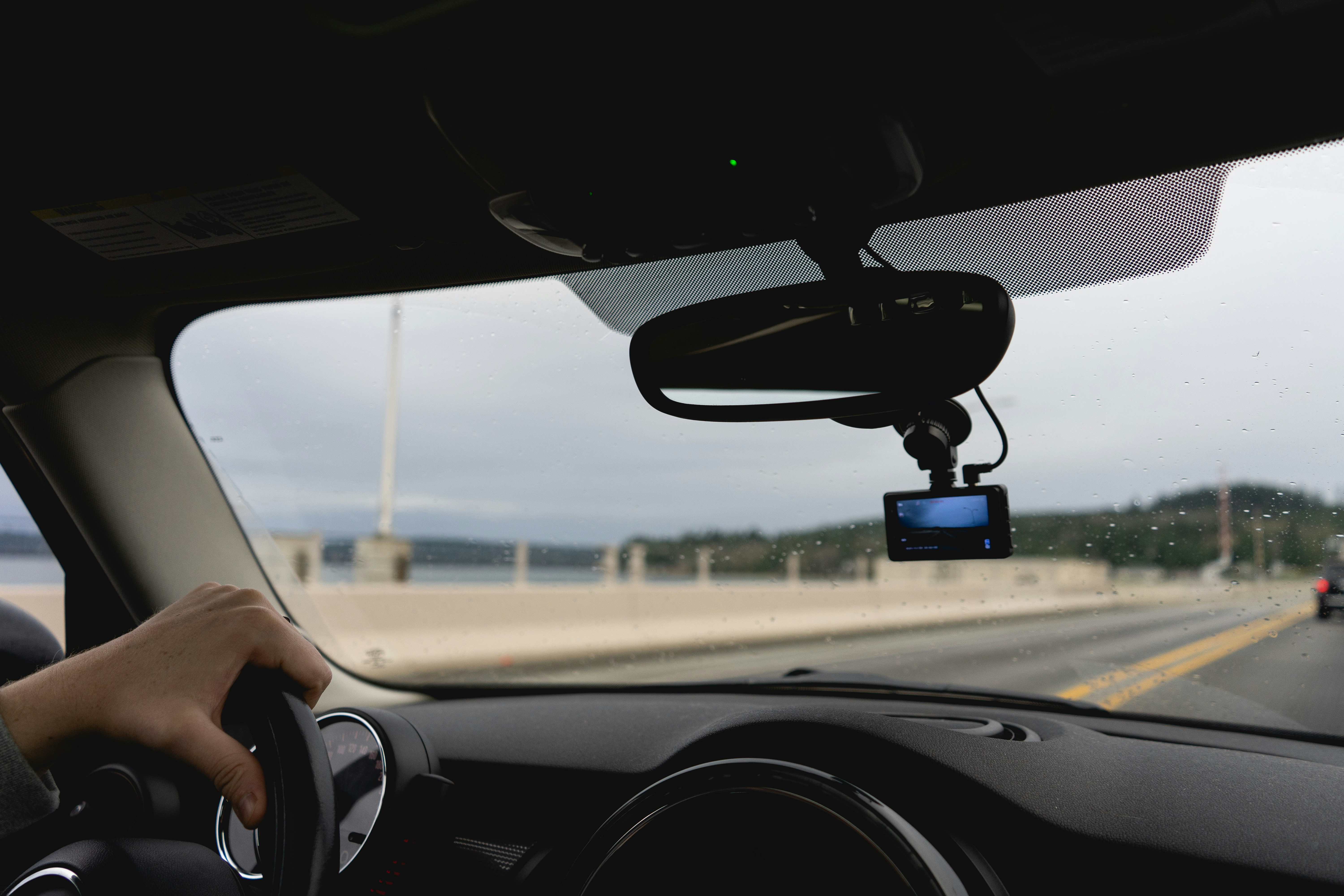 The car's windshield with a dash cam under the rear view mirror. 