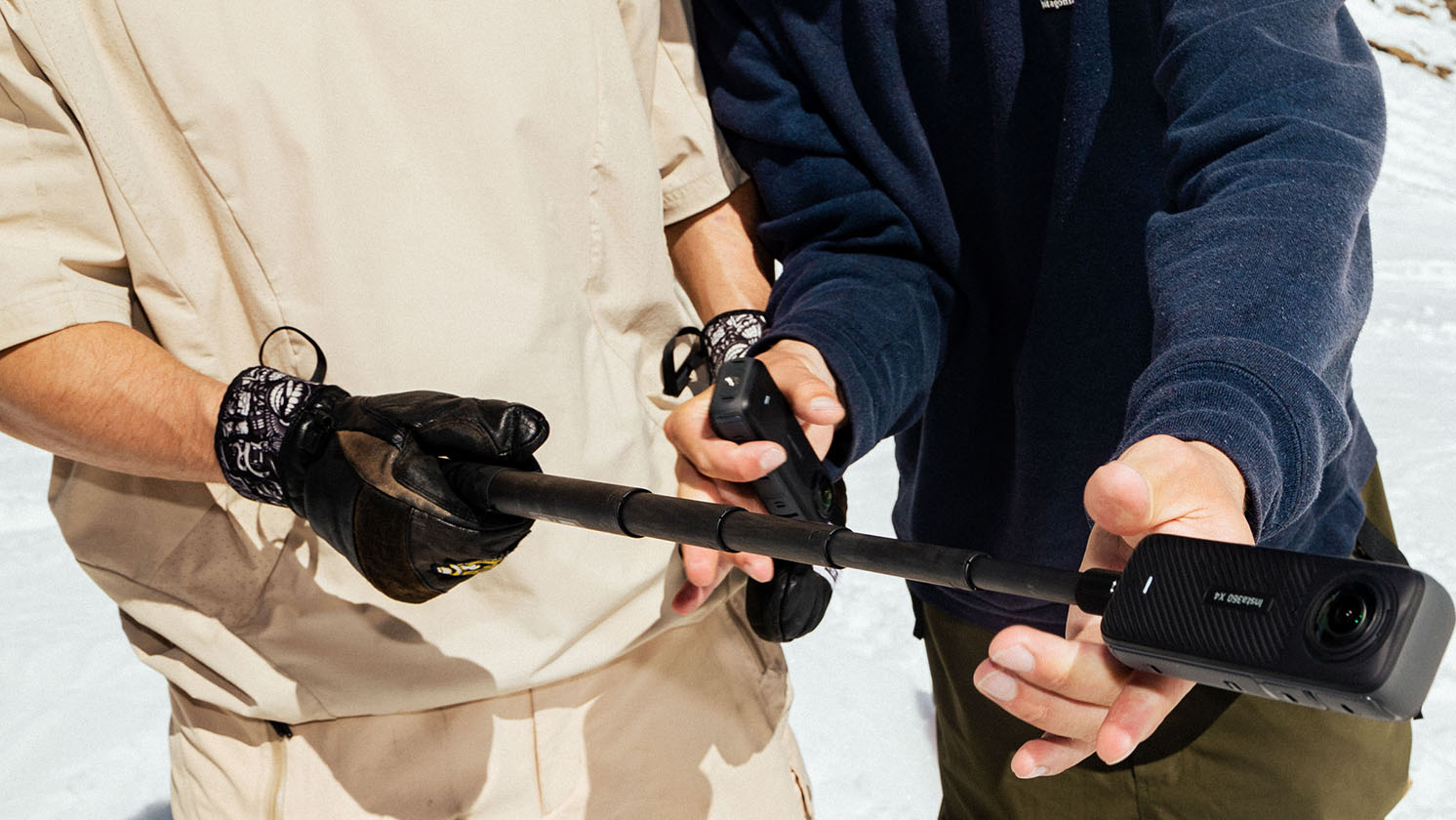 Two professional skiers inspect an Insta360 X4 on an extended invisible selfie stick during the Swatch Nines event in Schiltorn.