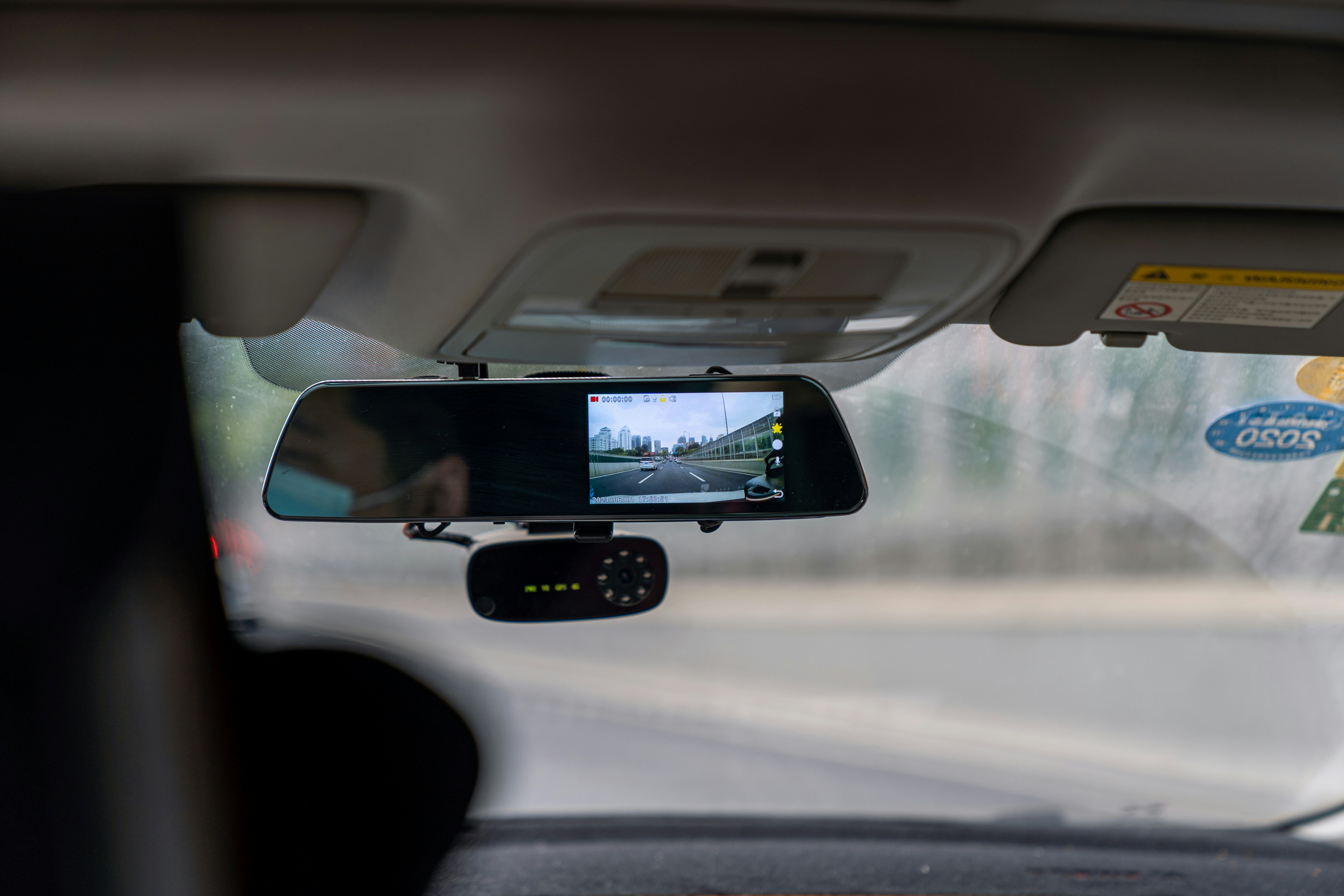 A close up of a car's interior. There is a car dash cam under the rear view mirror.