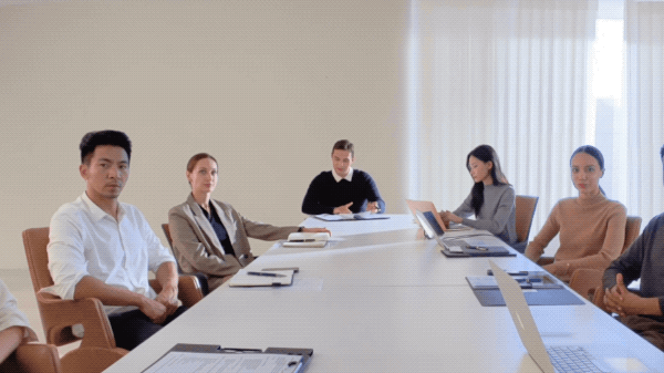 A group of people in a meeting. The camera zooms in on one man at the end of the table as he is speaking.