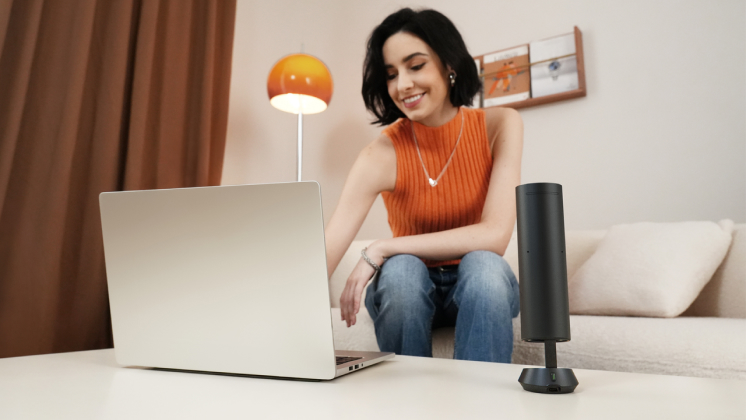 A woman uses a laptop in a lounge with Insta360 Wave, AI speakerphone nearby.