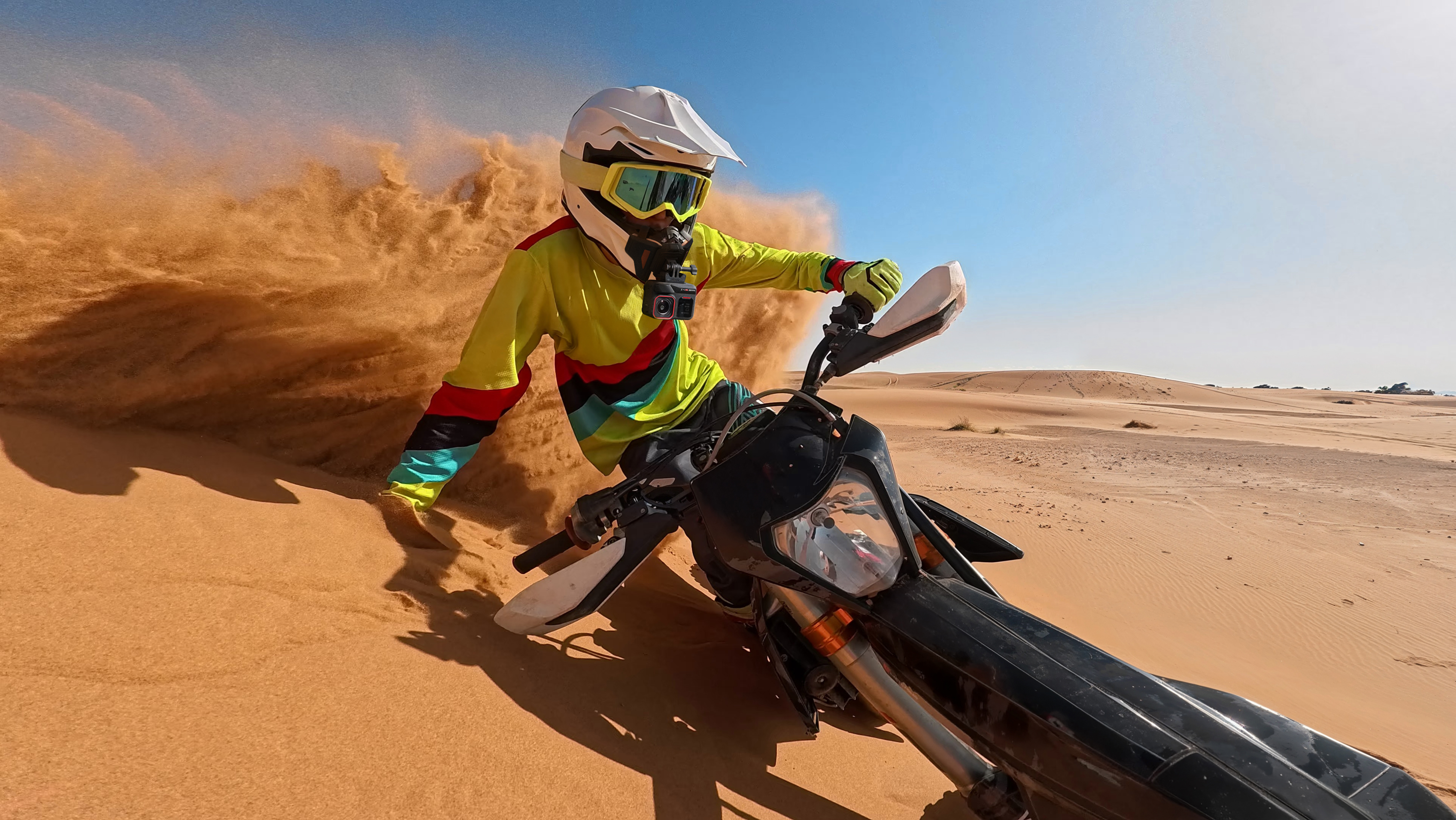 Insta360 Ace Pro 2 mounted on the chin of a motorcyclist's helmet. The motorcyclist is riding in the desert leaving a dust trail behind.