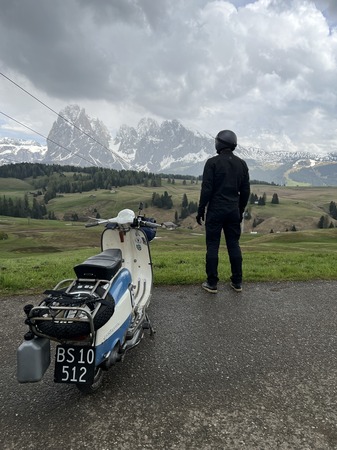 A man standing next to his Vespa looking out at the Alps.