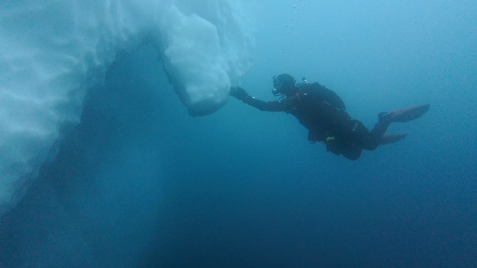 A diver next to an iceberg underwater.